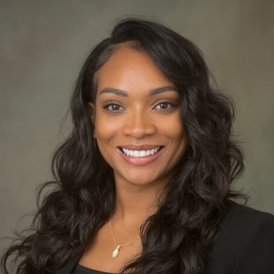 Smiling Black woman with long wavy dark hair wearing a black blazer and gold necklace.